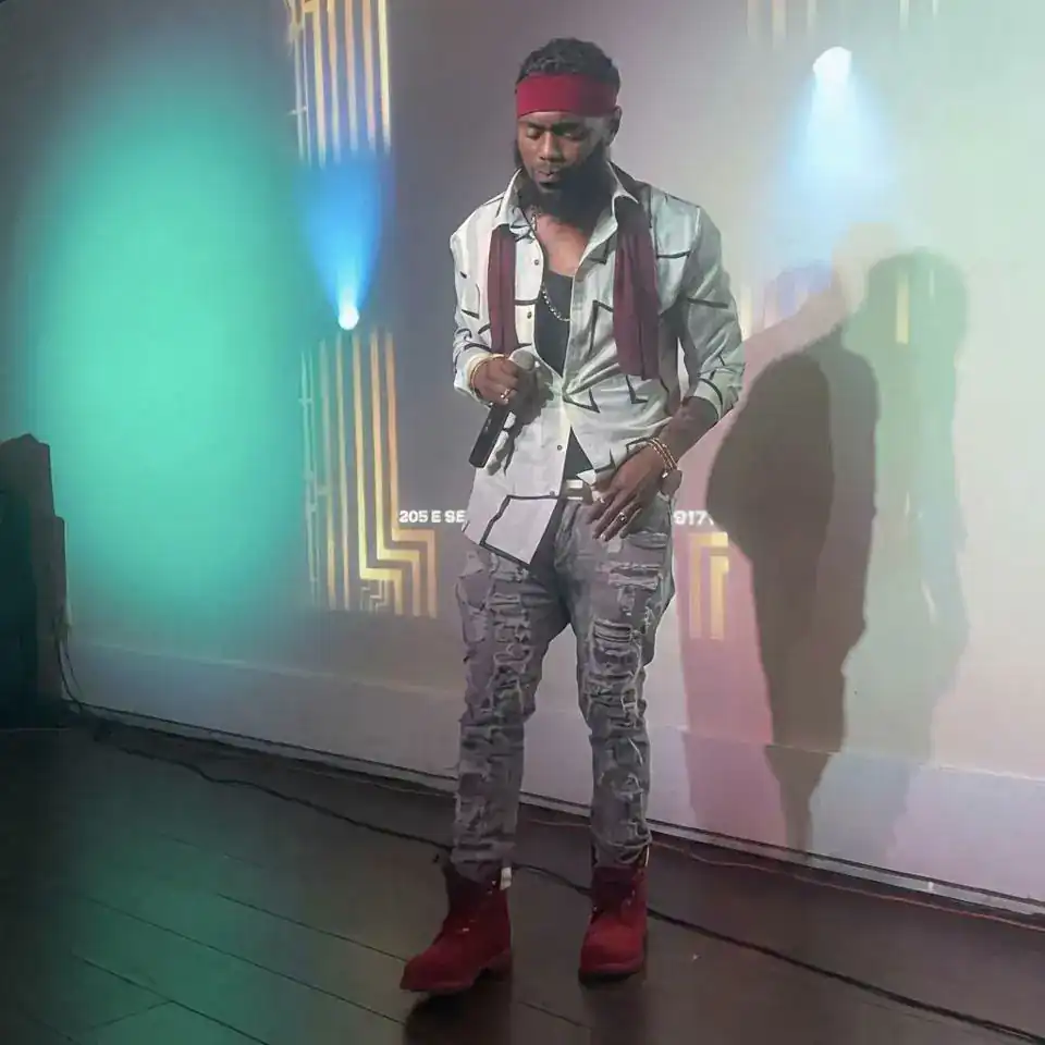 KingJu1c3 on stage holding a microphone, white jacket and red boots
