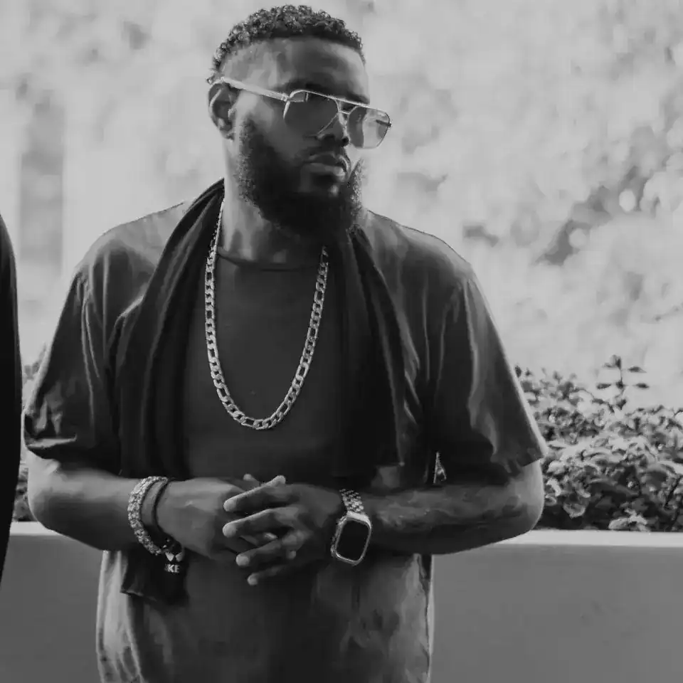 KingJu1c3 in black and white with aviator sunglasses and a gold chain, hands clasped