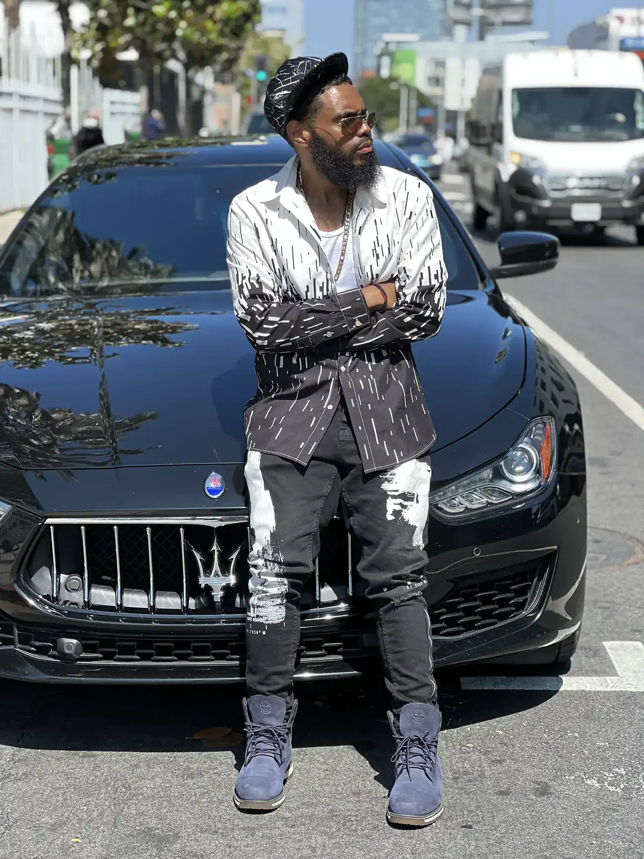 KingJu1c3 leaning on a black Maserati on a city street, arms crossed