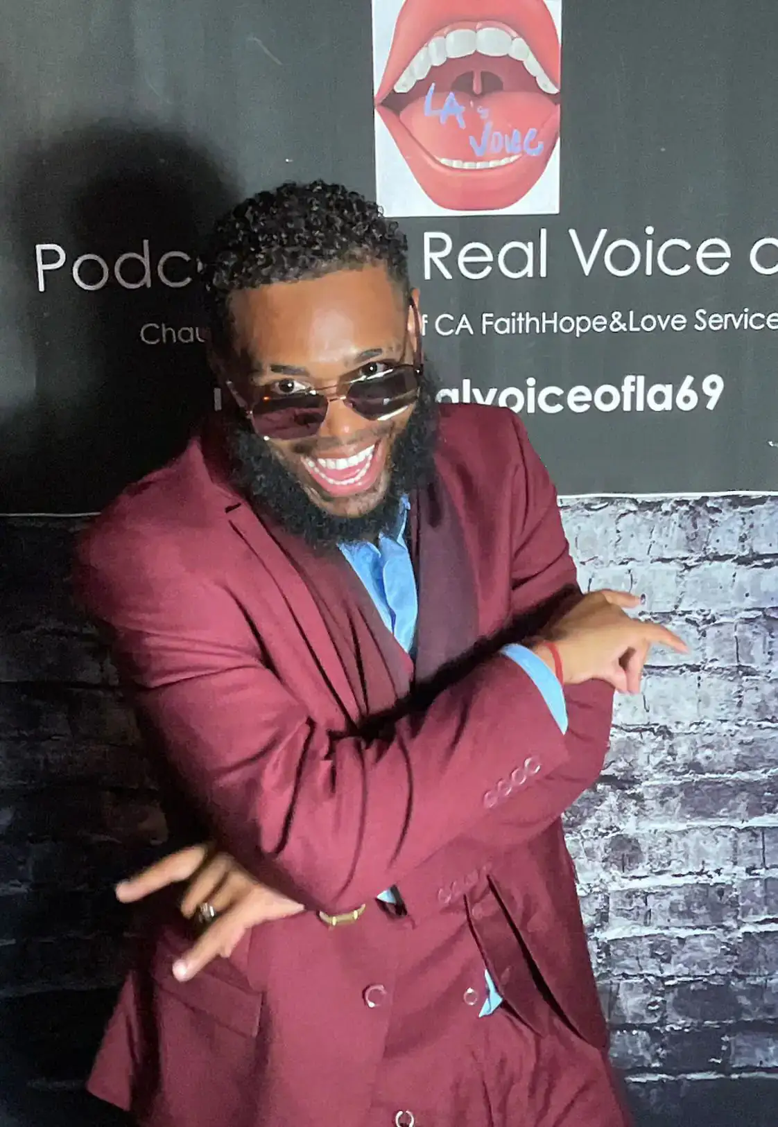 KingJu1c3 laughing in a burgundy suit in front of a podcast backdrop